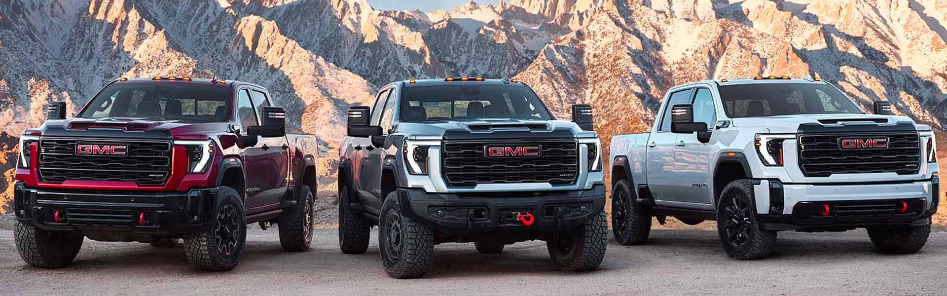Three 2025 GMC Sierra 2500 HD vehicles parked near mountain